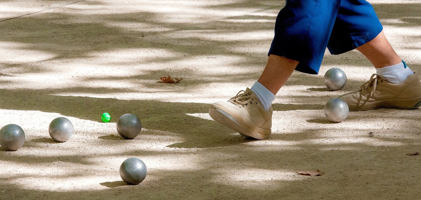 Boules de pétanque au sol avec le pied d'un joueur dans le cercle de lancer